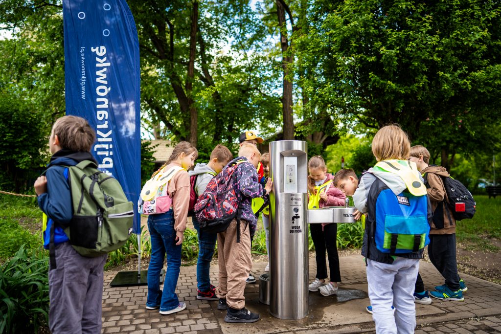 Na zdjęciu dzieci w wieku szkolnym przy urządzeniu, które dystrybuuje darmową wodę do picia