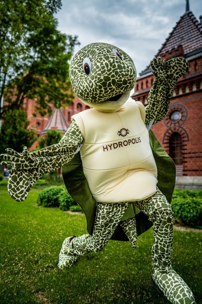 Na zdjęciu bardzo duża maskotka w kształcie żółwia z napisem na brzuchu Hydropolis. Jest to strój, w który przebrał się człowiek